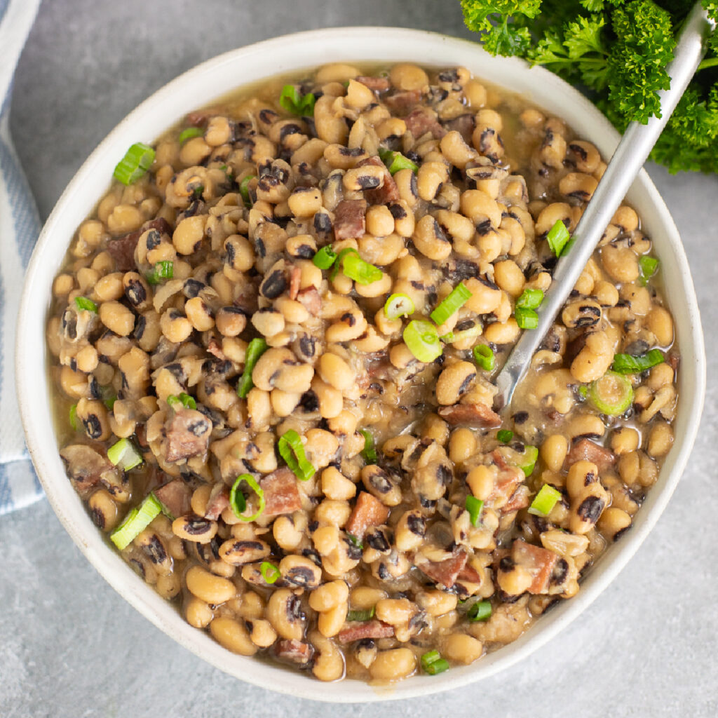 Overhead view of Instant pot black-eyed peas in a white bowl topped with sliced green onions and a spoon in the middle.
