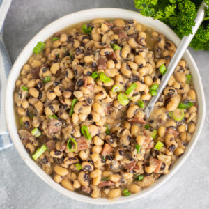 Overhead view of Instant pot black-eyed peas in a white bowl topped with sliced green onions and a spoon in the middle.
