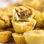 A stack of pecan tassies with a bite taken out of the top one with more tassies behind.