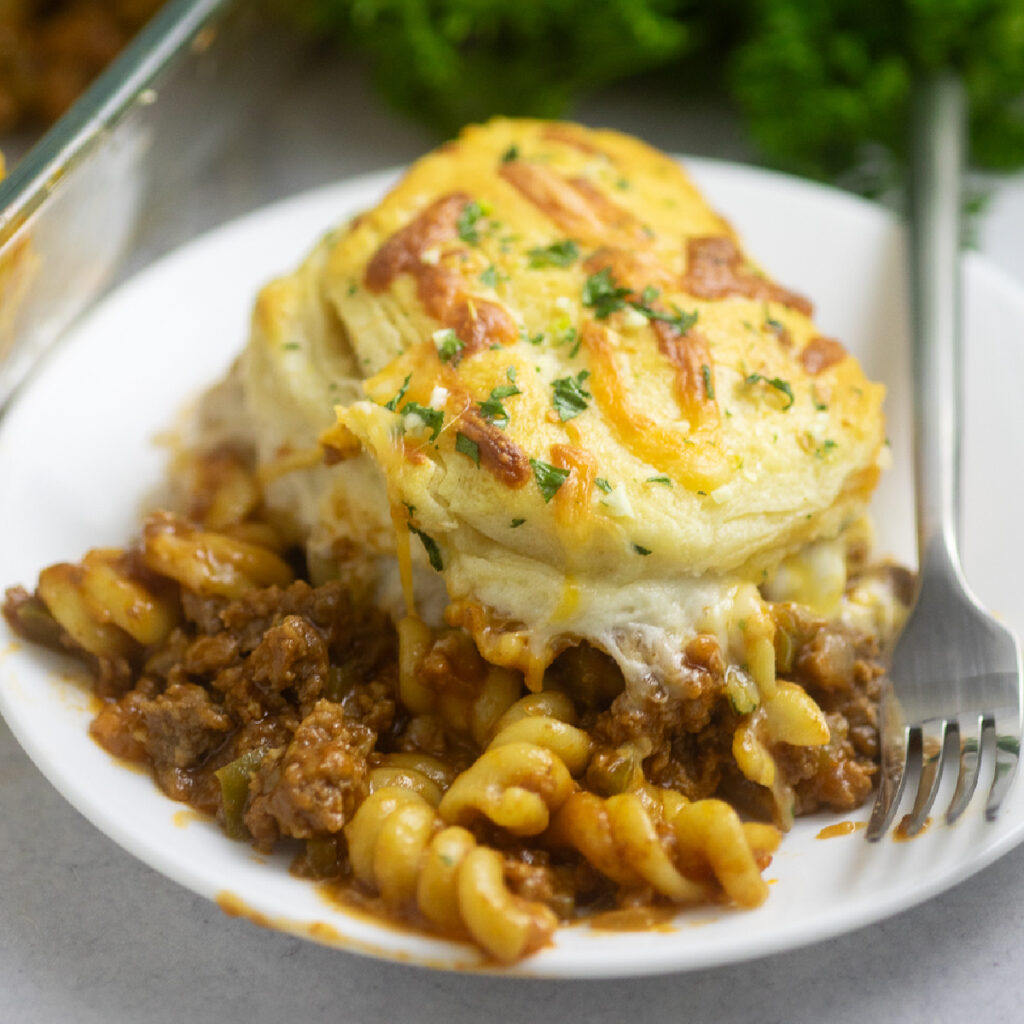 A serving of sloppy joe casserole topped with fresh parsley on a small plate next to a fork.