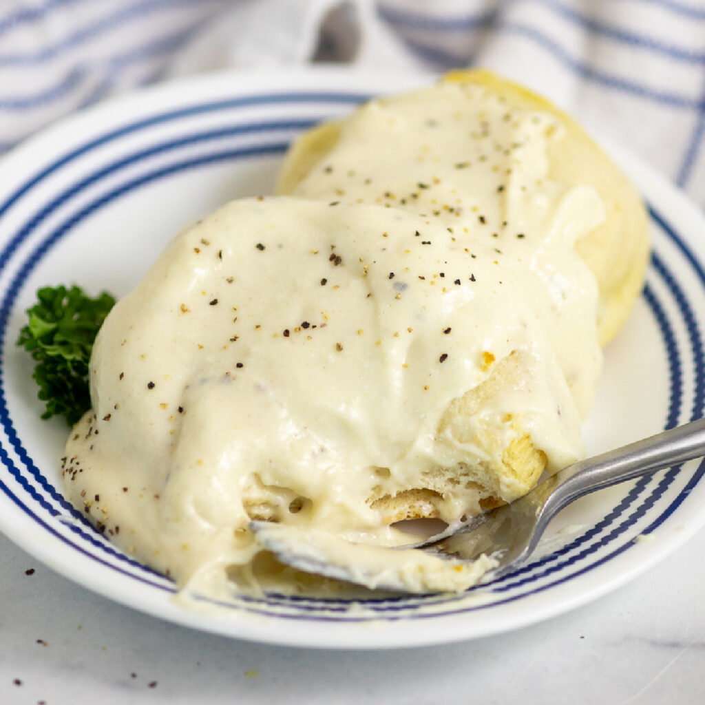 A biscuit split in half topped with country white gravy and black pepper with a fork sitting in front.