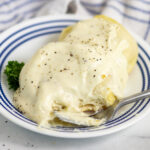 A biscuit split in half topped with country white gravy and black pepper with a fork sitting in front.