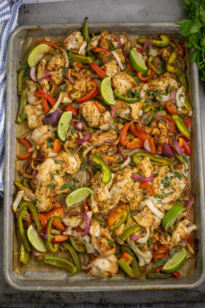 Sheet pan chicken fajitas on a sheet pan with lime wedges and fresh cilantro on top