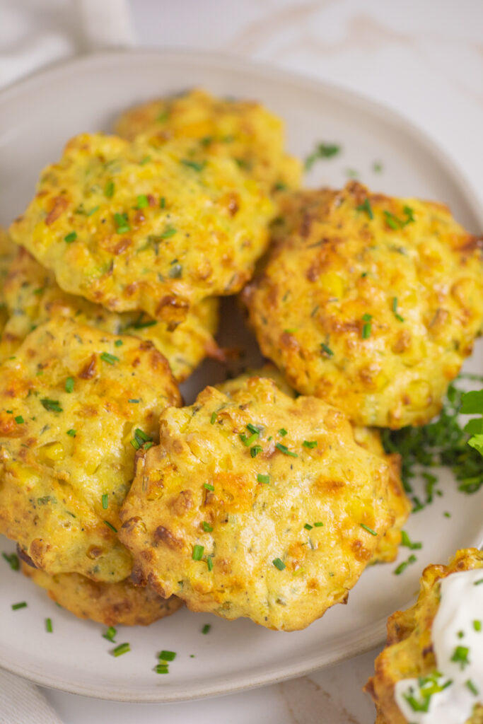 An overhead view of air fryer corn fritters piled on a white ceramic plate.