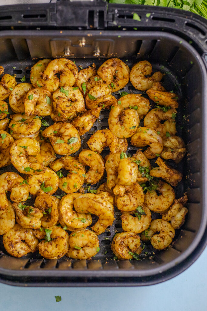 Cooked and seasoned shrimp in the air fryer basket with fresh cilantro for tacos.