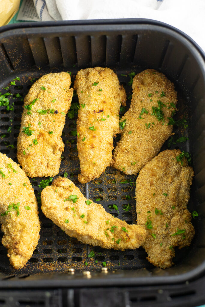 Overhead view of air fryer chicken tenders in an air fryer basket topped with freshly chopped parsley.