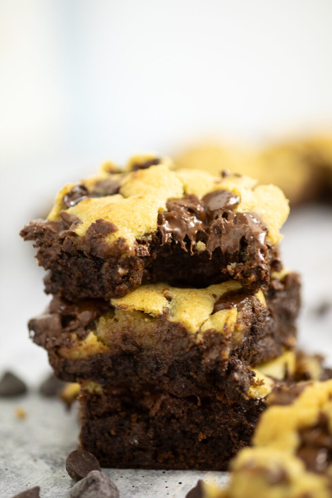 Stack of three brookies with a bite taken out of the top one and surrounded by chocolate chips.