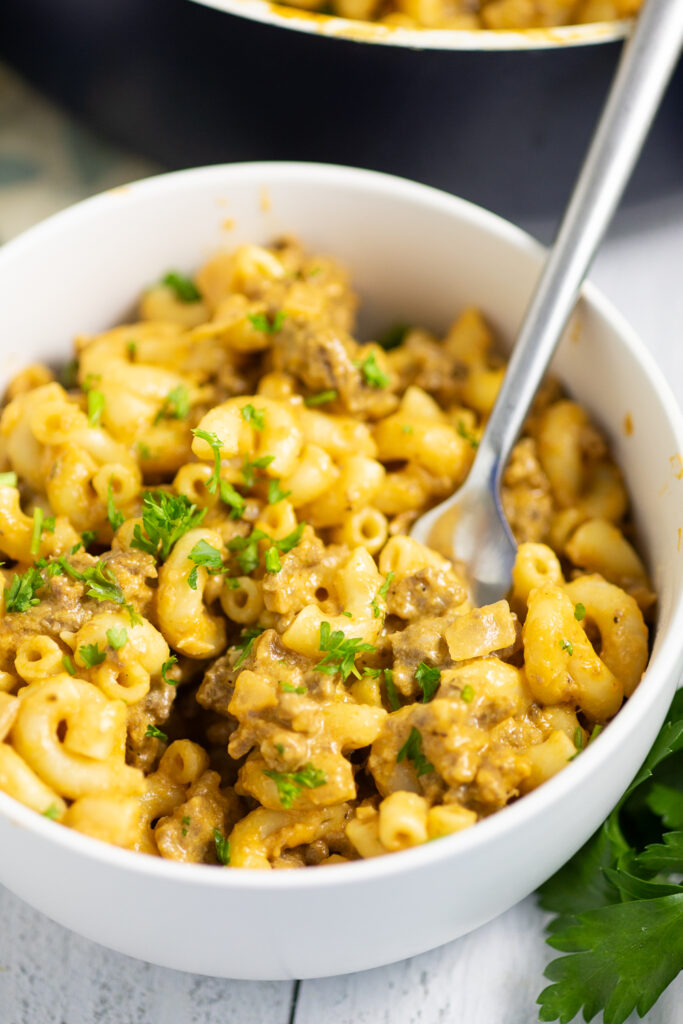 Overhead view of homemade hamburger helper in a white bowl topped with fresh parsley with a fork in it.