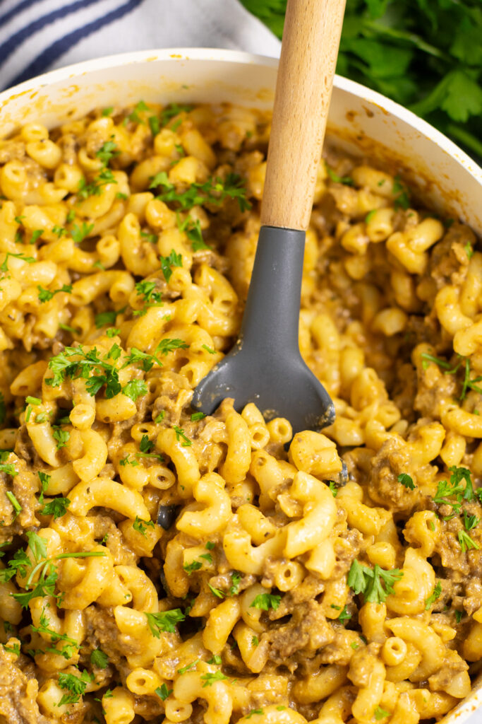 Overhead view of homemade hamburger helper in a large skillet with a wooden spoon sticking out of it.