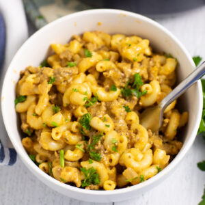 Overhead view of homemade hamburger helper in a white bowl with a fork in it, topped with fresh parsley.