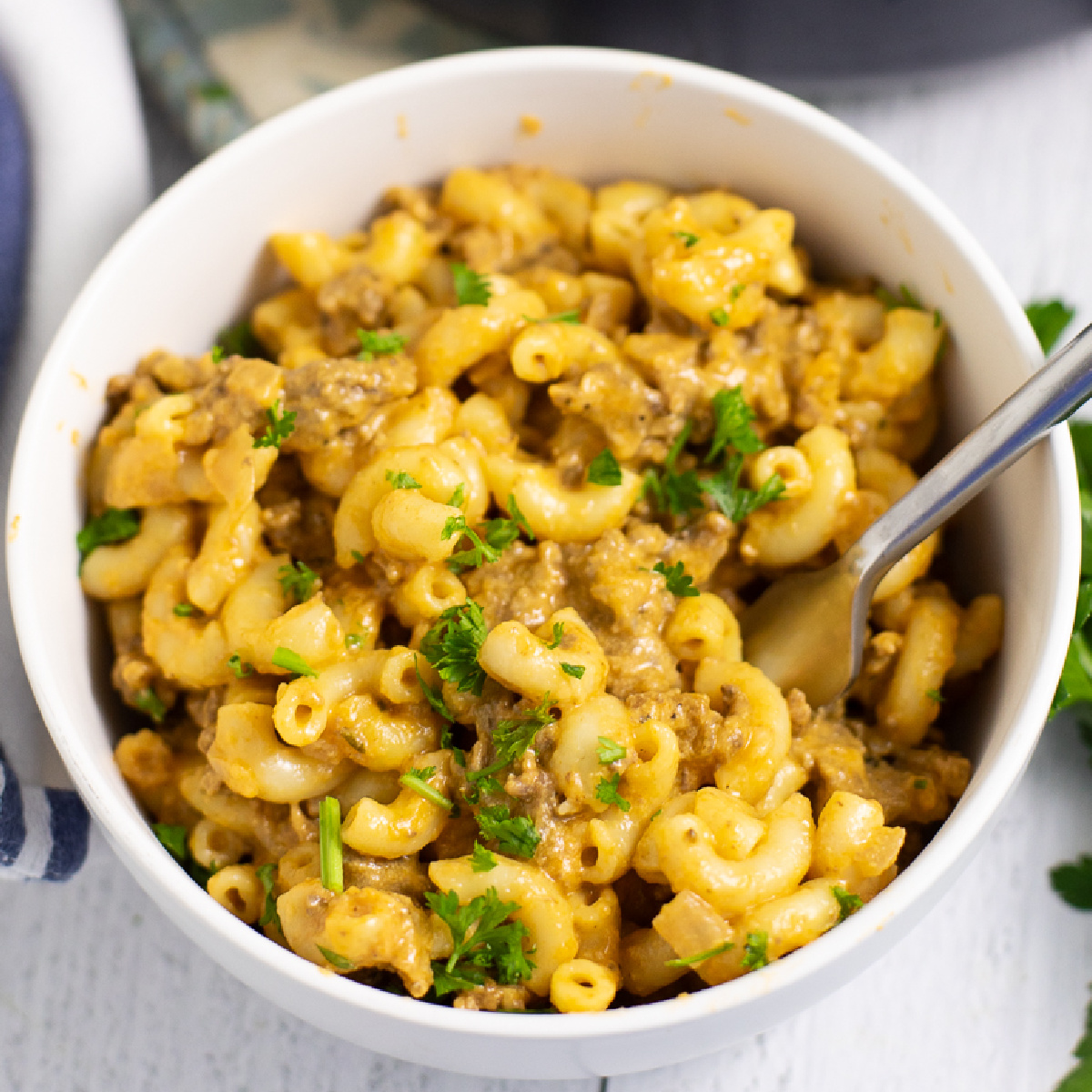 Overhead view of homemade hamburger helper in a white bowl with a fork in it, topped with fresh parsley.