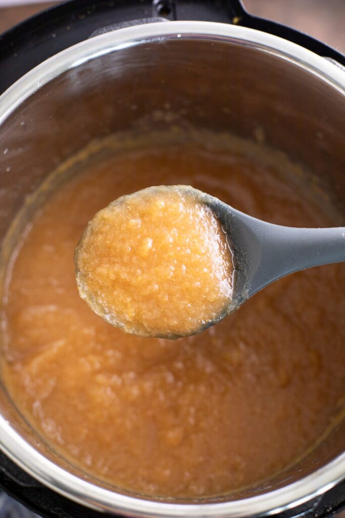 A large silicone spoon taking a scoop of instant pot applesauce straight out of the instant pot.