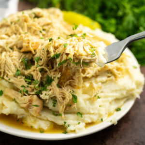 Crockpot Mississippi Chicken on top of mashed potatoes topped with fresh parsley with a fork taking a bite out of it.