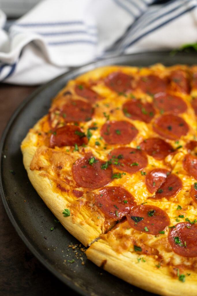 Close up of a homemade pepperoni pizza with homemade pizza crust cut into slices with a linen napkin behind.