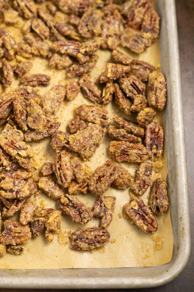 Candied pecans on a parchment paper lined metal baking sheet.