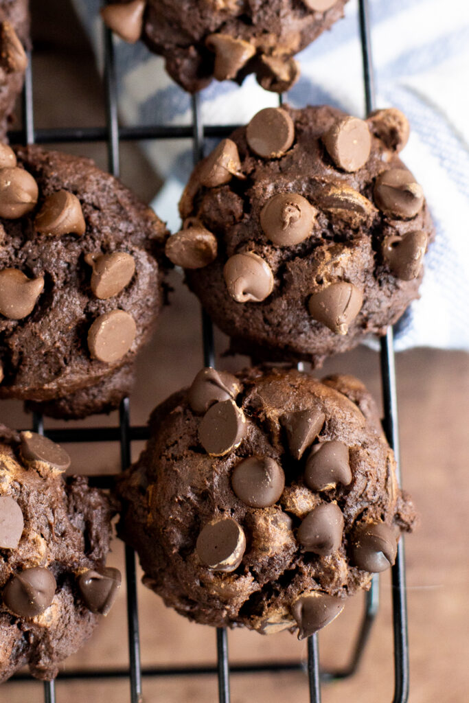 Overhead view of double chocolate pumpkin cookies on a cooling rack over a rustic metal background.