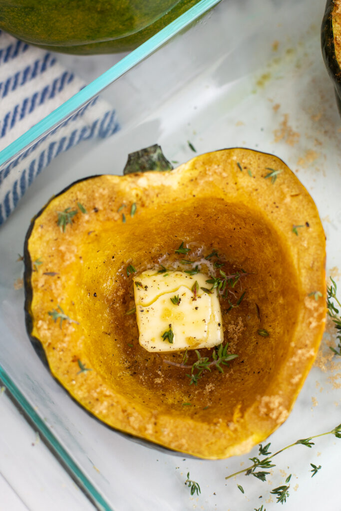 Overhead view of half of a cooked microwave acorn squash topped with a pat of butter and fresh thyme.
