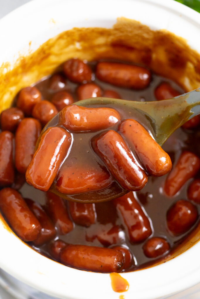 Overhead view of a spoon lifting slow cooker little smokies from a Crock Pot.