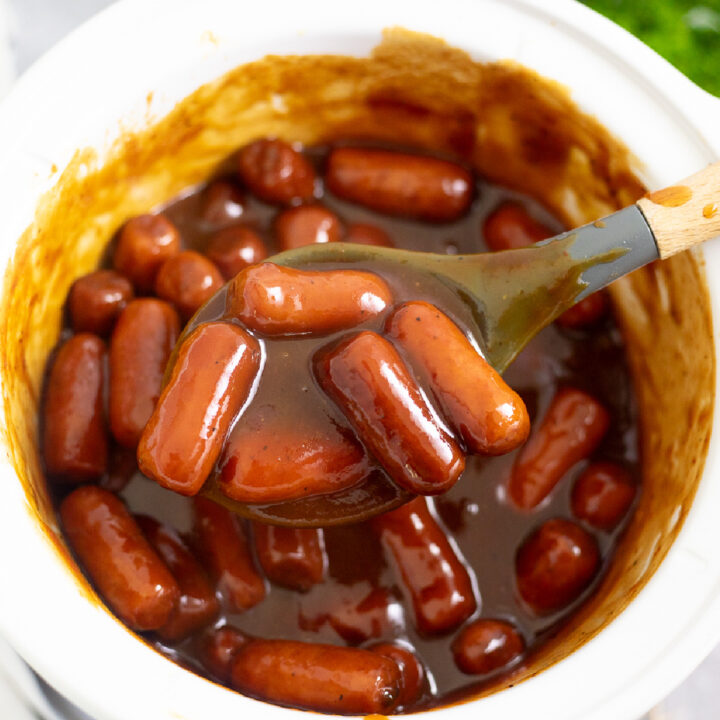 Overhead view of a spoon lifting slow cooker little smokies from a Crock Pot.