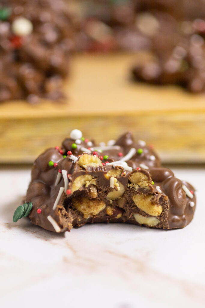 Crockpot Christmas Candy with a bite taken out sitting on a white marble background with a wood cutting board behind.
