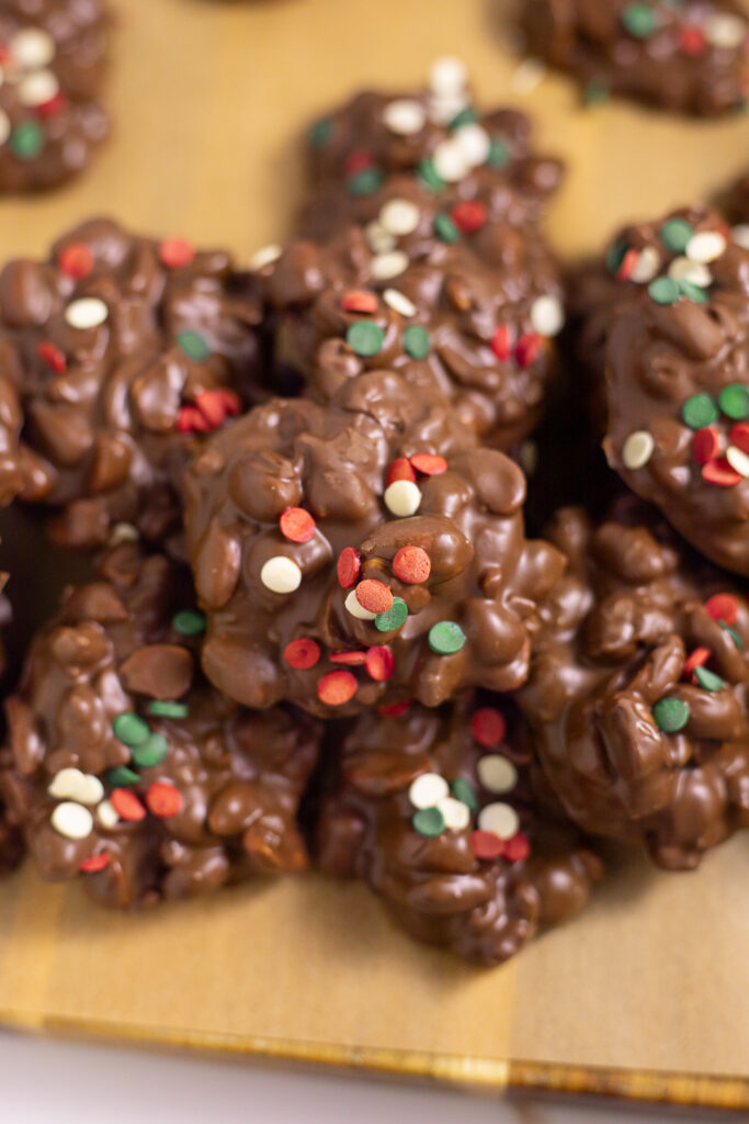 Overhead view of a pile of Crockpot Christmas Candy on brown parchment paper topped with holiday sprinkles.