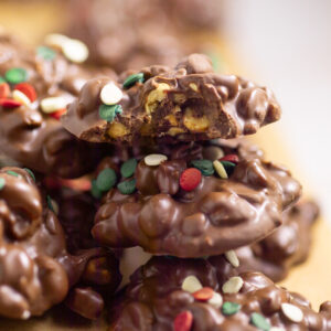 A pile of Crockpot Christmas Candy with topped with holiday sprinkles with a bite taken out of the top candy.