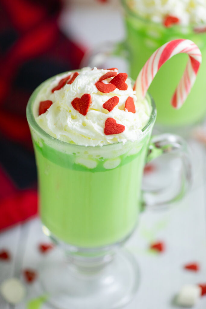 Close up of the whipped cream and red heart sprinkles on top of green Grinch hot chocolate.
