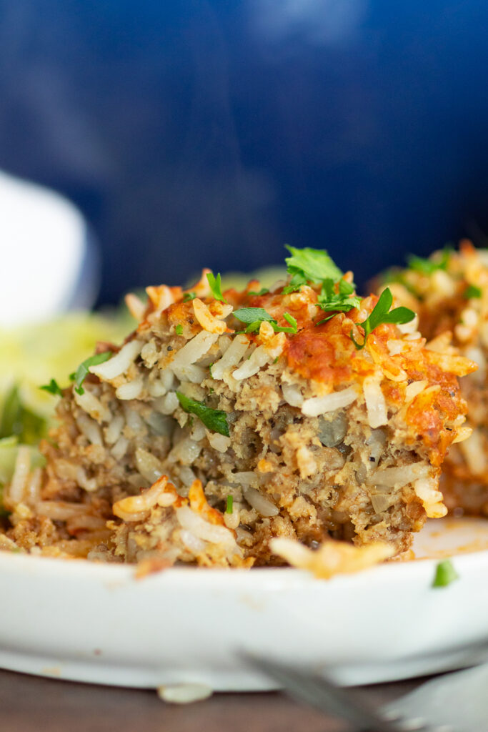 A porcupine meatball cut in half to show the rice and inside, on a white plate with the Dutch oven behind it.