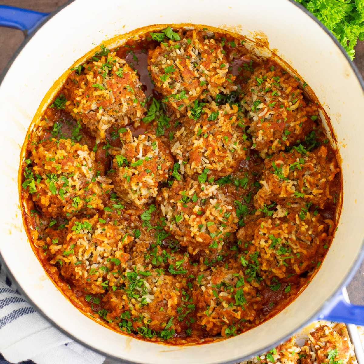 Overhead view of porcupine meatballs in a Dutch oven with red sauce and topped with fresh parsley.