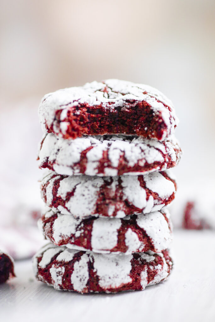 A stack of red velvet crinkle cookies with a bite taken out of the top one.