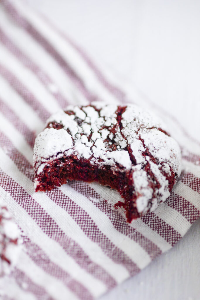 A red velvet crinkle cookie with a bite taken out of it on a red and white striped linen napkin.