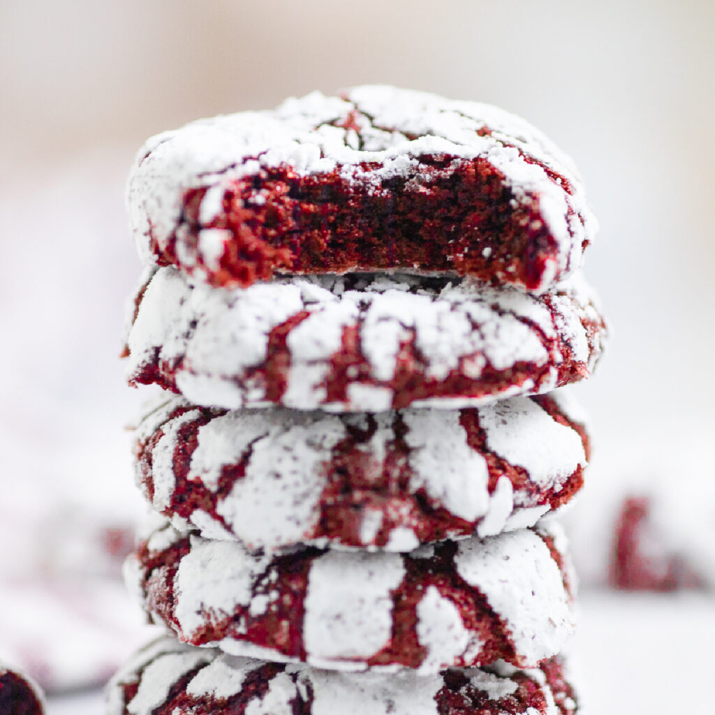A stack of red velvet crinkle cookies with a bite taken out of the top one.