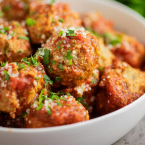 Close up of crockpot turkey meatballs in a white bowl topped with grated parmesan and fresh parsley.