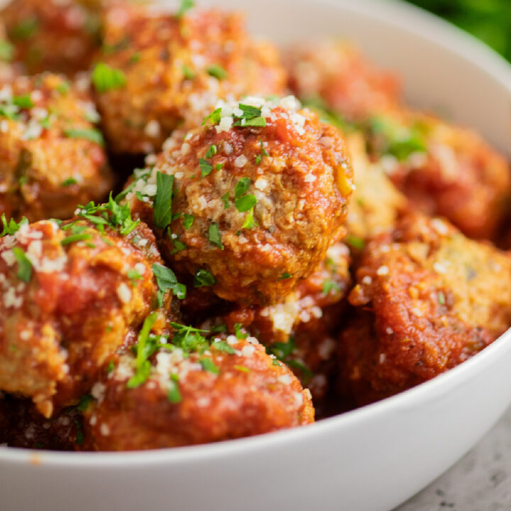 Close up of crockpot turkey meatballs in a white bowl topped with grated parmesan and fresh parsley.