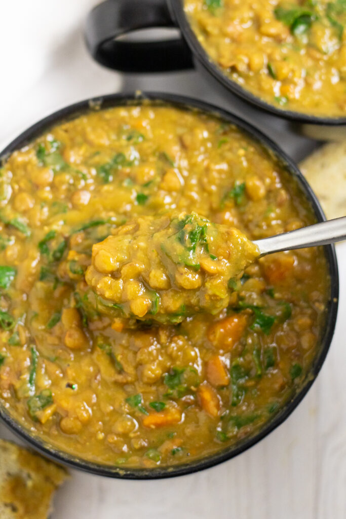 Overhead view of a black matte bowl filled with instant pot lentil soup with a spoon picking up a bite from the center, and a second bowl of soup above.