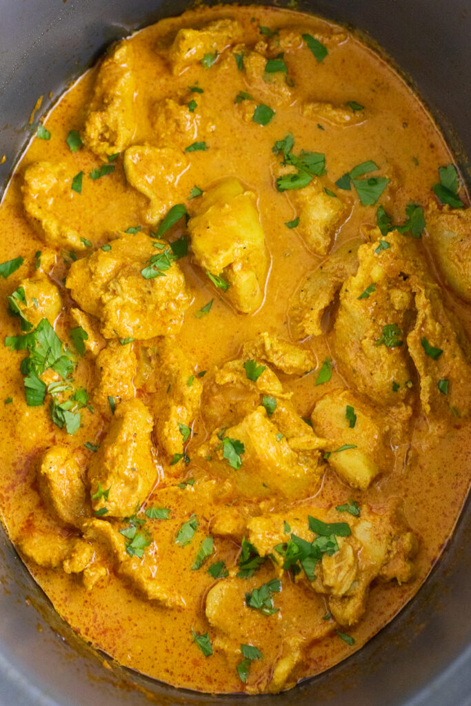 Overhead view of chicken tikka masala in a crockpot topped with fresh cilantro.