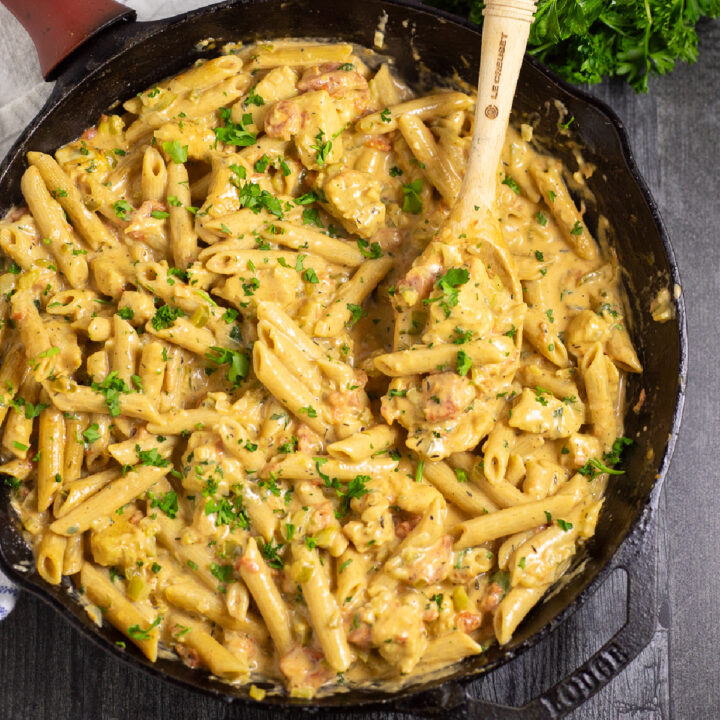 Overhead view of Creamy Cajun Chicken Pasta in a cast iron skillet topped with fresh parsley with a spoon in the middle. Skillet is on a dark rustic wood background next to a bunch of parsley.
