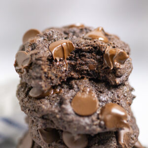 A stack of double chocolate chip cookies with a bite taken out of the top one.