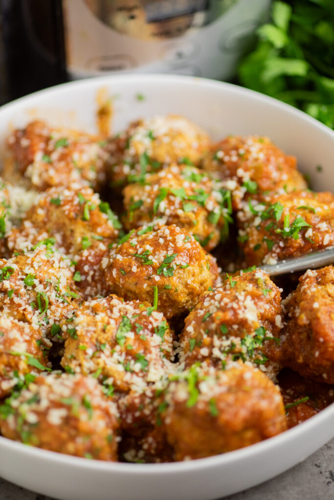 Crockpot turkey meatballs in red sauce topped with parmesan and fresh parsley in a white bowl with a metal spoon in the middle.