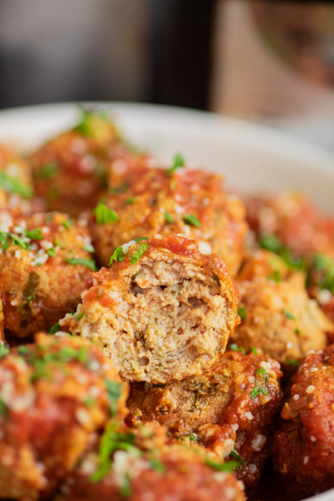 Close up of a crockpot turkey meatball with a bite taken out in a pile of meatballs.