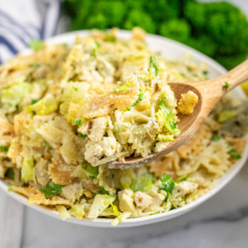 Chicken caesar pasta salad in a white bowl, topped with shredded parmesan with a wooden spoon taking out a scoop.