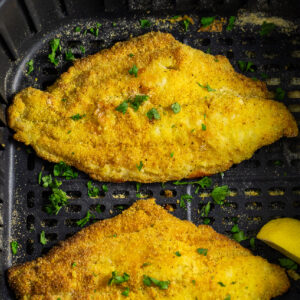 Air fryer catfish filet topped with fresh parsley in an air fryer basket.