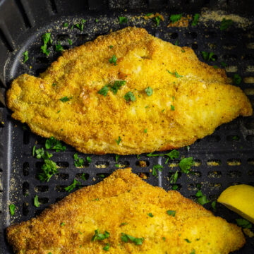 Air fryer catfish filet topped with fresh parsley in an air fryer basket.