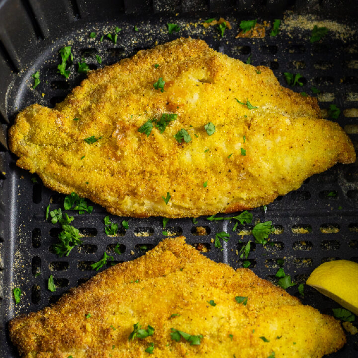 Air fryer catfish filet topped with fresh parsley in an air fryer basket.