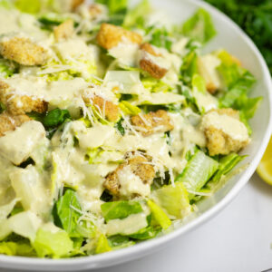 Side view of a caesar salad with homemade caesar dressing, shredded parmesan and croutons in a wide white bowl.