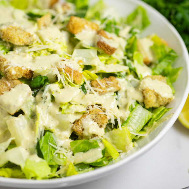 Side view of a caesar salad with homemade caesar dressing, shredded parmesan and croutons in a wide white bowl.