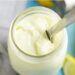 Homemade mayo in a mason jar with a butter knife scooping some out, with lemons and an immersion blender in the background